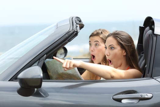 Amazed girls in a car pointing away on summer vacations