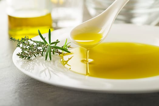 Healthy olive oil with herbs pouring with spoon close up
