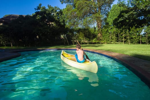 Boy swimming pool water with kayak canoe paddle playing childhood.