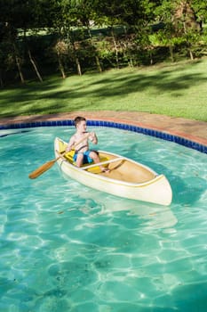 Boy swimming pool water with kayak canoe paddle playing childhood.