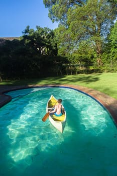 Boy swimming pool water with kayak canoe paddle playing childhood.