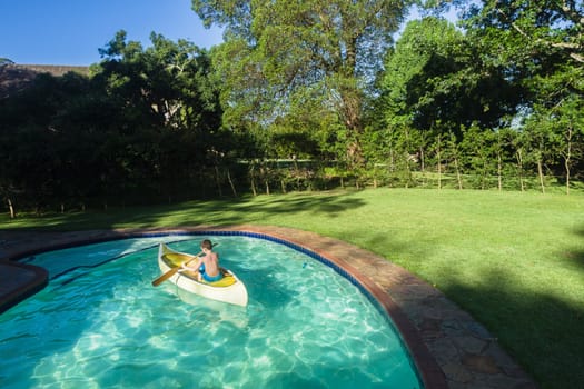 Boy swimming pool water with kayak canoe paddle playing childhood.