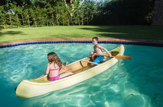 Children boy girl summer playtime in swimming pool waters with  kayak canoe paddles