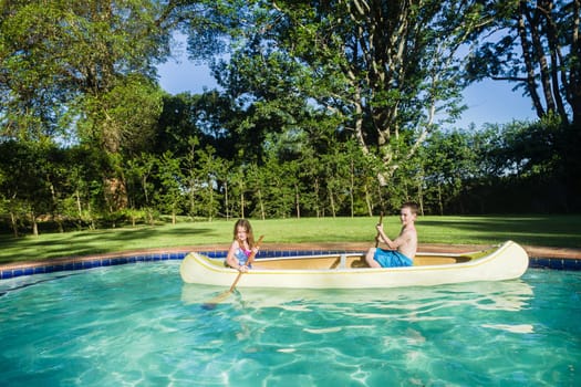 Children boy girl summer playtime in swimming pool waters with  kayak canoe paddles
