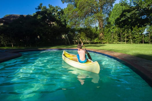 Boy swimming pool water with kayak canoe paddle playing childhood.