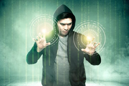 Young asian hacker in black hoodie touching virtual screen with binary code over green background
