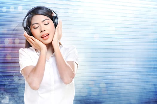 Pretty asian woman in white shirt listening music with headphones over white roller shutter door with smoke and colorful light reflection background