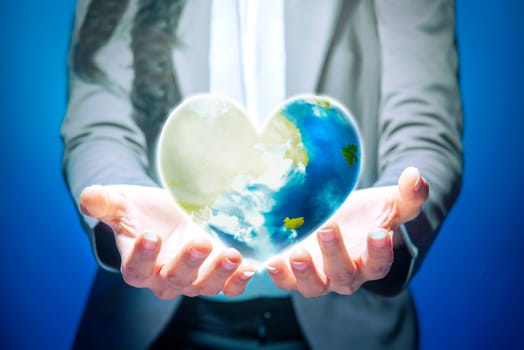 Business woman standing with open palm holding the earth with heart shape using her both hands over blue background. Earth day concept