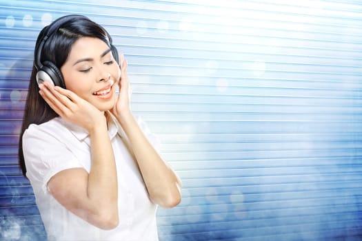Pretty asian woman in white shirt listening music with headphones over white roller shutter door with smoke and colorful light reflection background