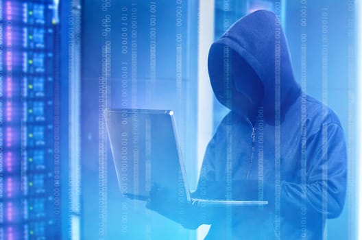 Hacker in black hoodie holding laptop with binary code on virtual screen with modern storage of server in the data center on the background