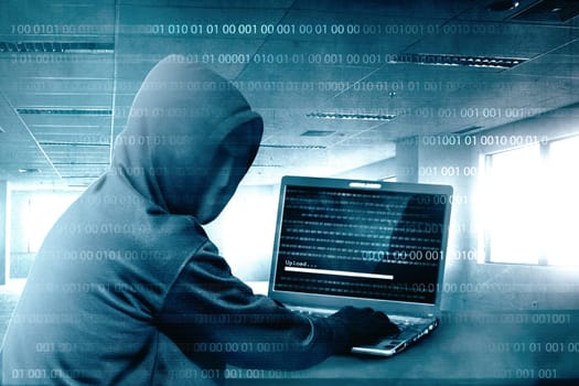 Hacker in black hoodie using laptop on the desk to hacking system with binary code and upload the malware inside the room