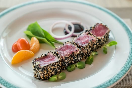 Seared tuna with sesame seeds with green salad on white plate
