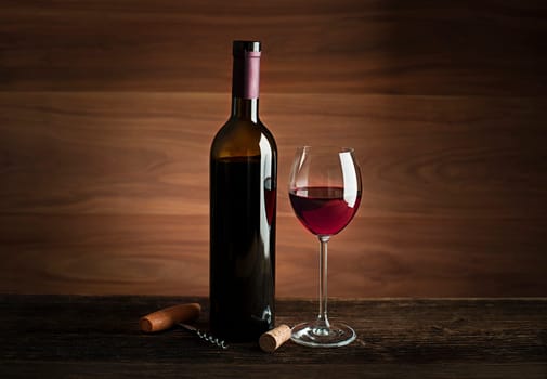 Glass and bottle of red wine on wooden background.