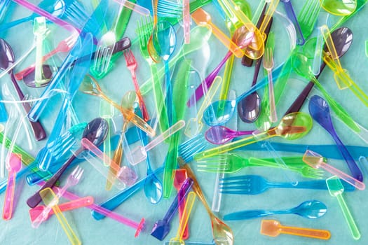 Variety of colorful plastic cutlery on blue background