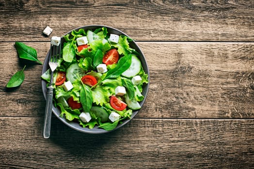 Salad with feta cheese and fresh vegetables on wooden background. Healthy food.