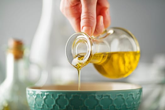 Bottle of virgin olive oil pouring to bowl close up