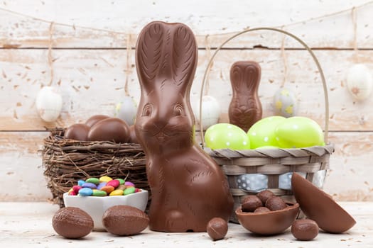 Delicious chocolate Easter bunny, eggs and sweets on rustic background