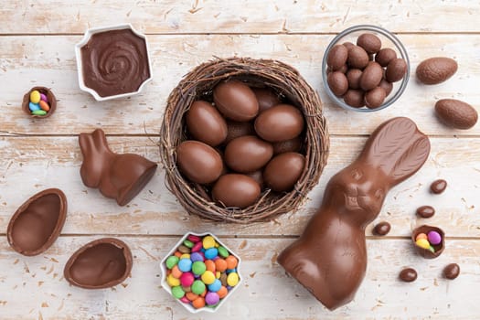 Delicious chocolate Easter bunny, eggs and sweets on rustic background