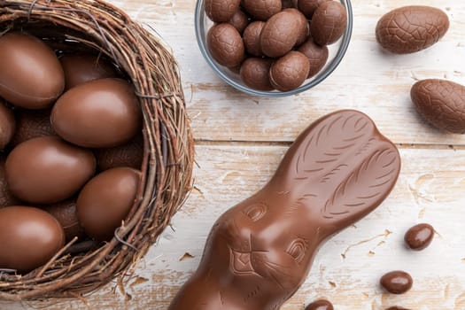 Delicious chocolate Easter bunny, eggs and sweets on rustic background
