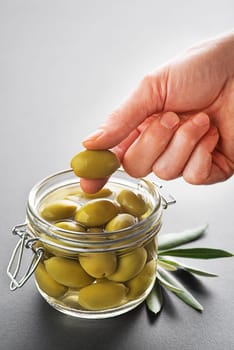 Pickled green olives in glass jar close up. Eating with hands.