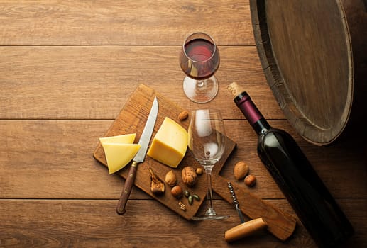 Bottle of red wine with wineglass and cheese on wooden and barrel background.