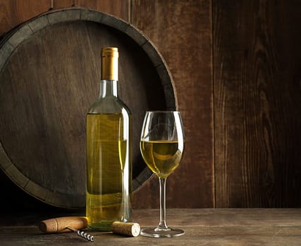 Bottle of white wine with wine glass on old board. Wine bottle and glass with barrel background.