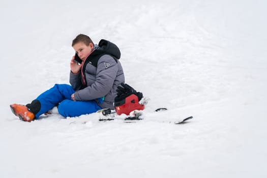 Szklarska Poreba, Poland - February 2019 : Young boy calling for help on his mobile phone after skiing or snowboarding accident on the mountain slope, Szrenica mountain, Karkonosze