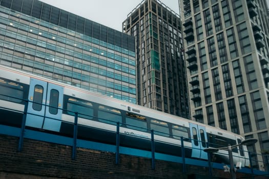 London, United Kingdon - November 2018 : City overground train with commuters going over the bridge with business office skyscrapers in the background