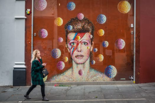 London, England - December 2018 : Woman walking in front of the graffiti in memory of singer David Bowie as Ziggy Stardust, Brixton