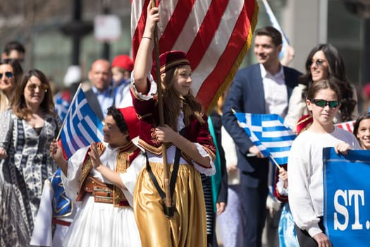 Chicago, Illinois, USA - April 29, 2018  Young greek woman wearing traditional clothing carrying the USA flag during the Greek Independence  Day Parade