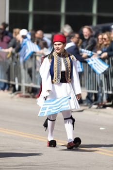 Chicago, Illinois, USA - April 29, 2018  Greek child wearing traditional clothing waving the greek flag during the Greek Independence  Day Parade