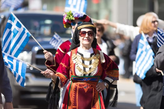 Chicago, Illinois, USA - April 29, 2018  Greek woman wearing traditional clothing waves the greek flag during the Greek Independence  Day Parade