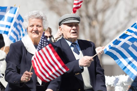 Chicago, Illinois, USA - April 29, 2018 Older Greek couple wave the USA and Greek flags during the Greek Independence  Day Parade