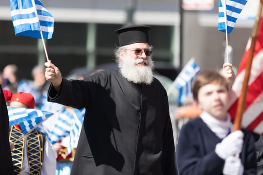 Chicago, Illinois, USA - April 29, 2018  An orthodox priest waves the greek flag during the Greek Independence  Day Parade