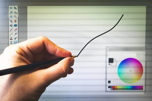 graphic editor softwares - an hand with a pencil draw on the computer screen .