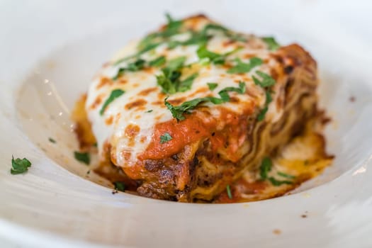 Portion of a delicious beef lasagne with melting cheddar, mozzarella and ricotta cheeses, garnished with parsley