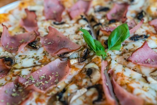 Close up of a freshly baked crispy ham and mushroom pizza decorated with basil leaf