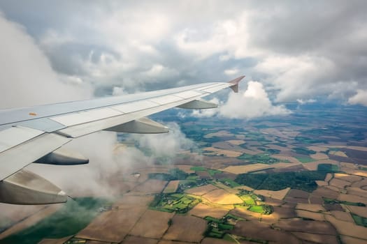 Window view of the wing of an airplane flying above the clouds and english countryside