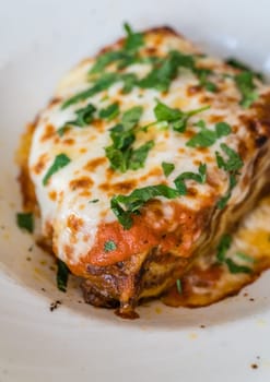 Portion of a delicious beef lasagne with melting cheddar, mozzarella and ricotta cheeses, garnished with parsley