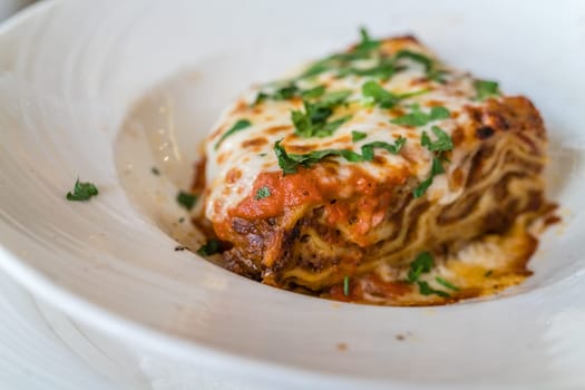 Portion of a delicious beef lasagne with melting cheddar, mozzarella and ricotta cheeses, garnished with parsley