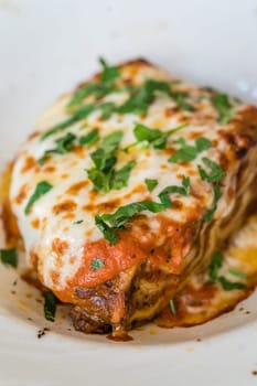 Portion of a delicious beef lasagne with melting cheddar, mozzarella and ricotta cheeses, garnished with parsley