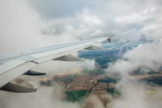Window view of the wing of an airplane flying above the clouds and english countryside