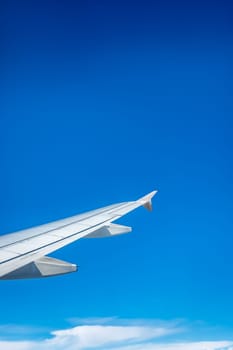 Window view of the wing of an airplane flying above the clouds