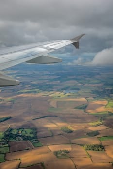 Window view of the wing of an airplane flying above the clouds and english countryside