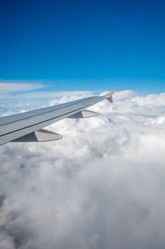 Window view of the wing of an airplane flying above the clouds
