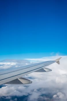 Window view of the wing of an airplane flying above the clouds
