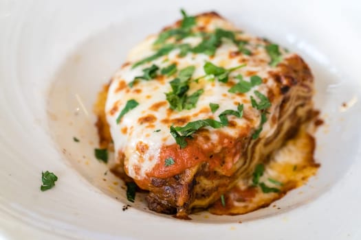 Portion of a delicious beef lasagne with melting cheddar, mozzarella and ricotta cheeses, garnished with parsley
