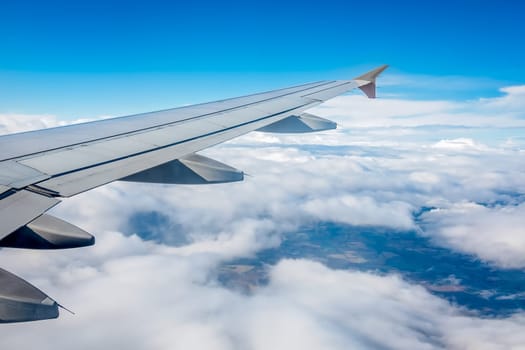 Window view of the wing of an airplane flying above the clouds