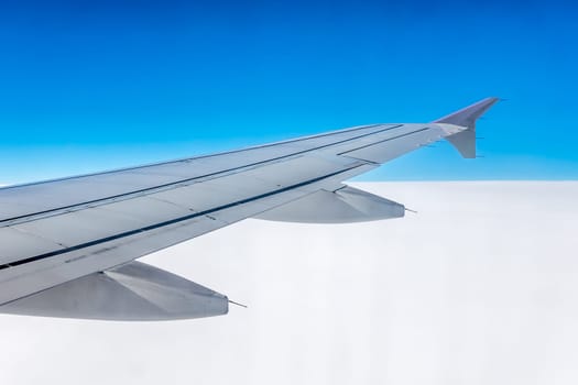 Window view of the wing of an airplane flying above the clouds