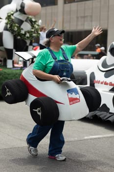 Indianapolis, Indiana, USA - May 26, 2018,  People with race car outfits walking along a float with a giant cow, promoting milk drinking, at the Indy 500 Parade